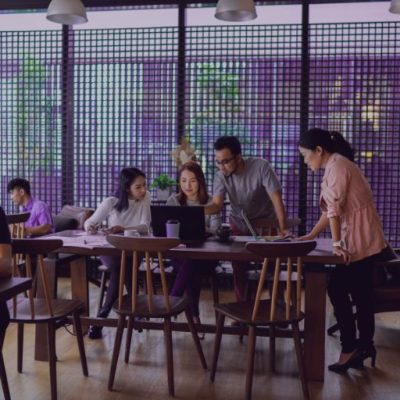 Ein Team, das um einen Tisch versammelt steht und gemeinsam auf einen Laptopbildschirm schaut, es repräsentiert Startup-Teams.