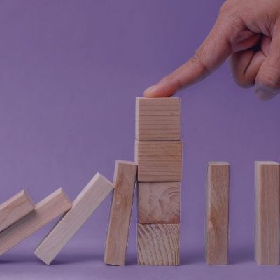 Ein Stapel Klötze, die umgefallen sind. Eine Hand stoppt den Fall und zeigt damit eine Problemintervention.