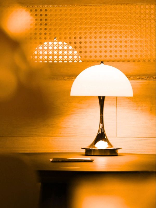 Eine Retrolampe auf einem Tisch vor einer Rattanwand.